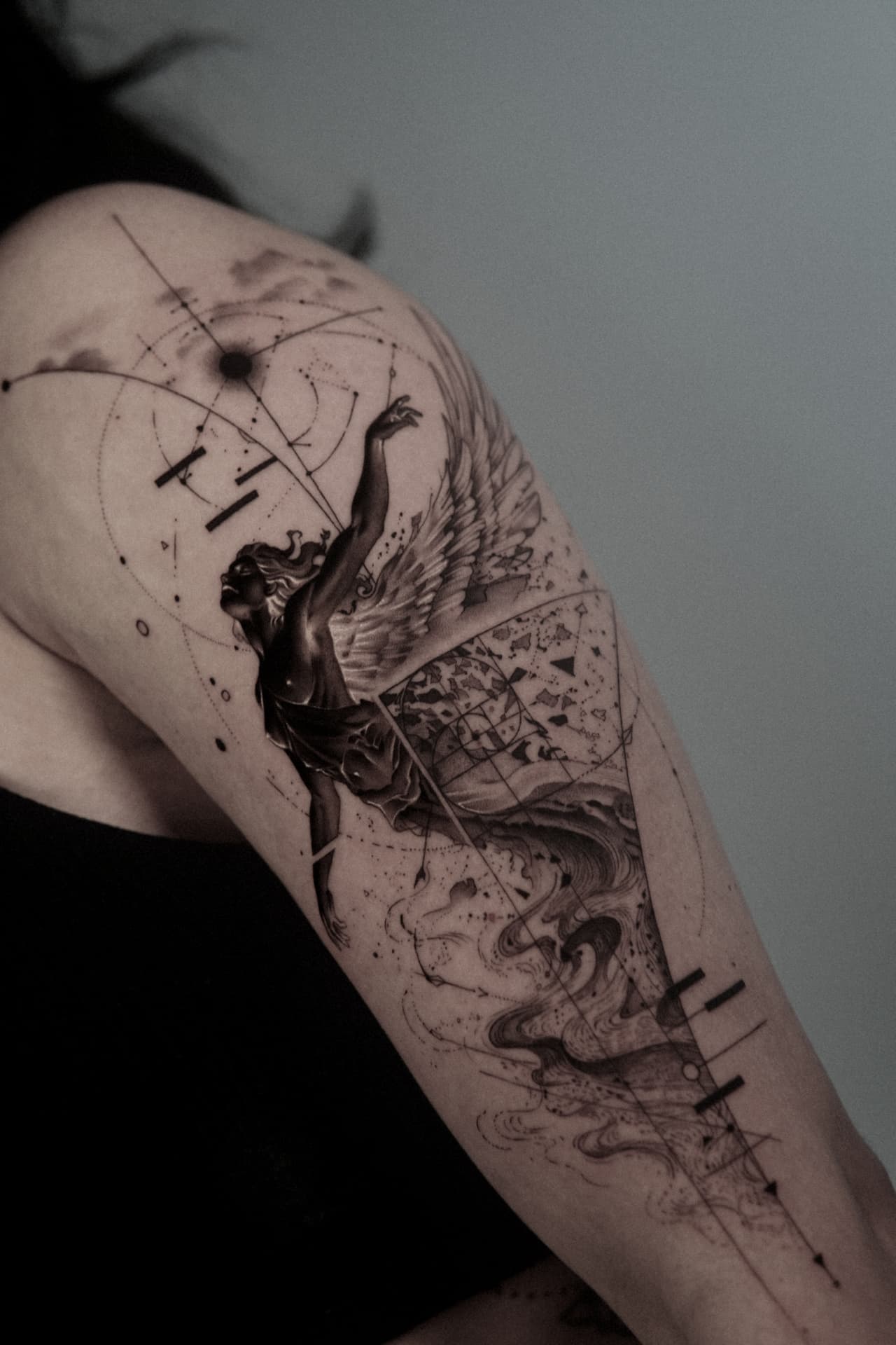 Tatuagem com figura alada, ondas e geometria no braço